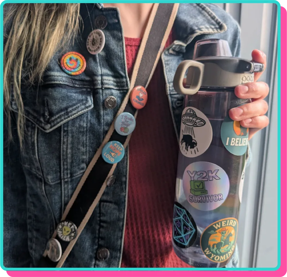 Denim jacket and bag strap covered in pins, holding a water bottle covered in stickers